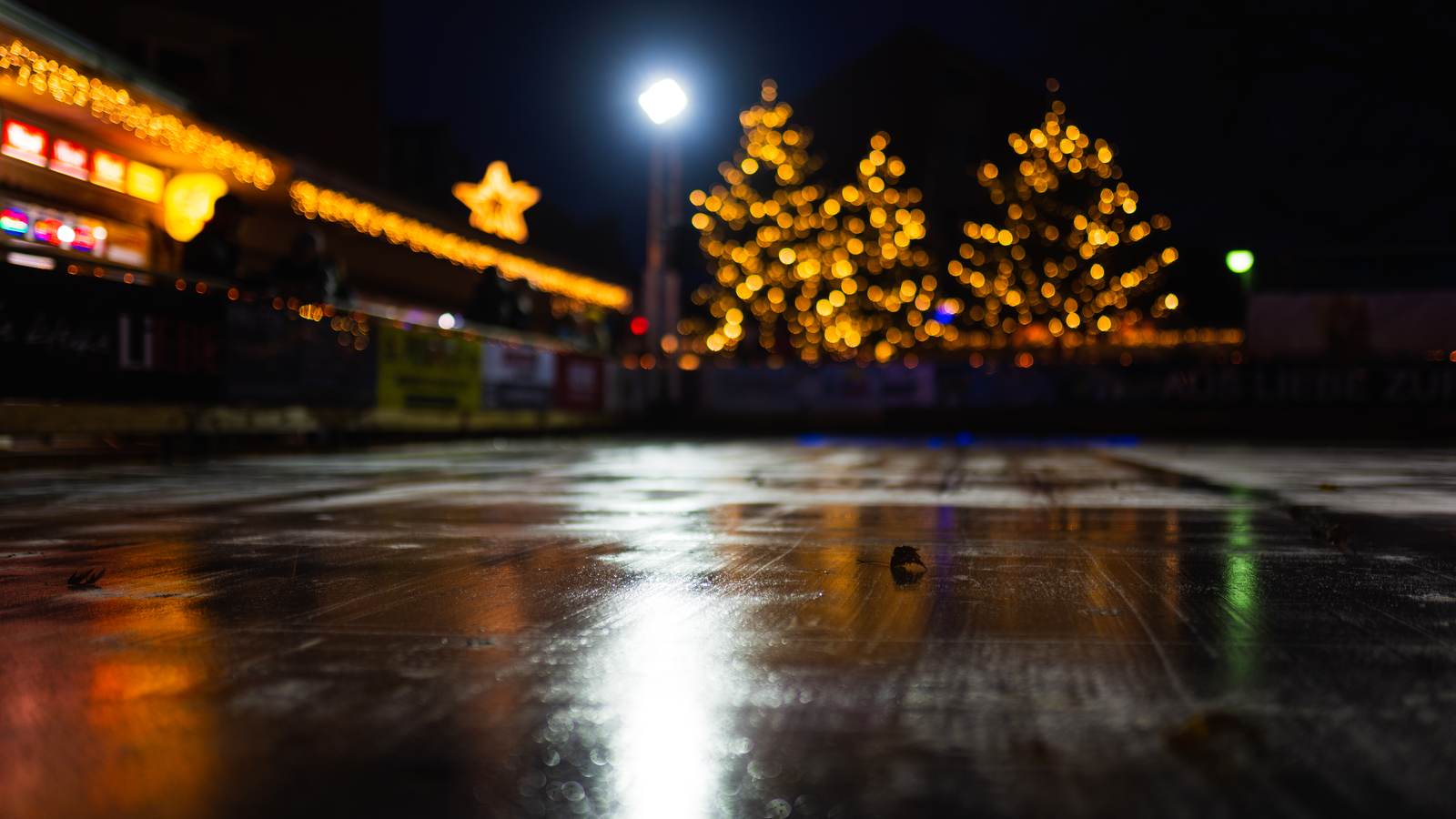 Winterabend in Elmshorn: beleuchtete Tannen und Lichterketten spiegeln sich auf der Eisfläche