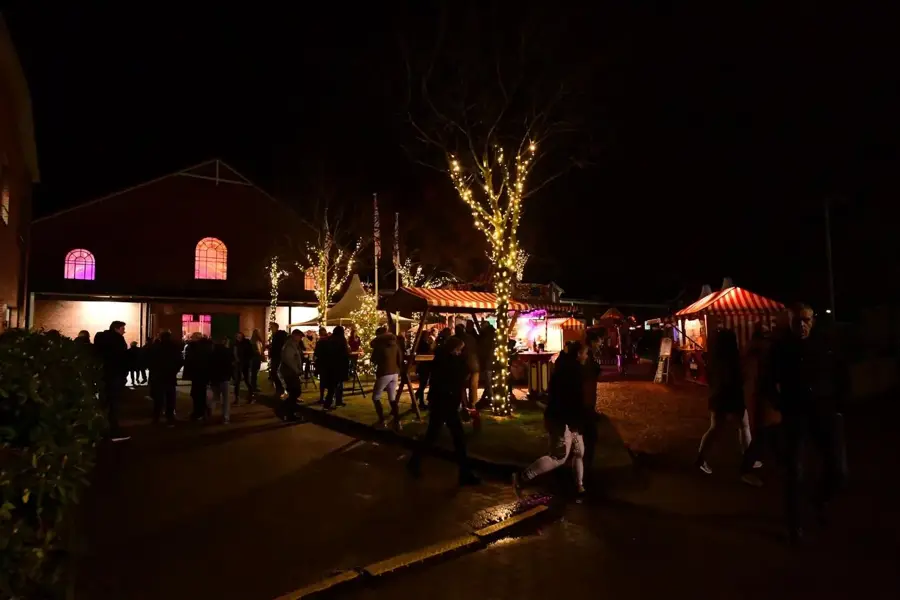 Weihnachtsmarkt vor der beleuchteten Backsteinfassade der Alten Reithalle bei Nacht mit Buden und Lichterketten